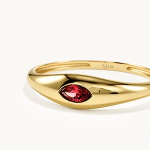 Könnte beinhalten: Ein polierter Goldring mit einer glatten, abgerundeten Ringschiene und einem horizontal in der Mitte gefassten, marquise-geschliffenen roten Edelstein. Die Innenseite des Rings ist deutlich mit 14K gekennzeichnet, was den Goldgehalt angibt.