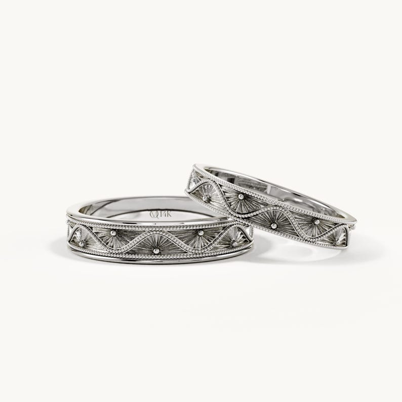 Pu&ograve; includere: Due anelli color argento caratterizzati da un motivo a onde ripetuto con sottili linee incise e piccoli accenti sferici. L'interno dell'anello pi&ugrave; largo &egrave; chiaramente stampigliato con il testo 14K, che indica la purezza del metallo dei gioielli.