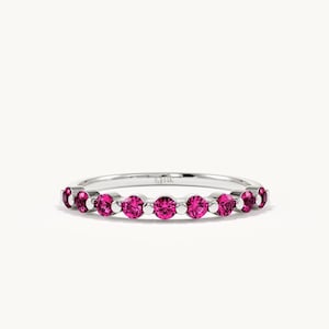 K&ouml;nnte beinhalten: Ein silberfarbener Ring mit einer Reihe von neun rund geschliffenen, leuchtend pinkfarbenen Edelsteinen in einer gemeinsamen Krappenfassung. Die Innenseite des Rings ist deutlich mit 14K graviert, was den Reinheitsgrad des Metalls angibt.