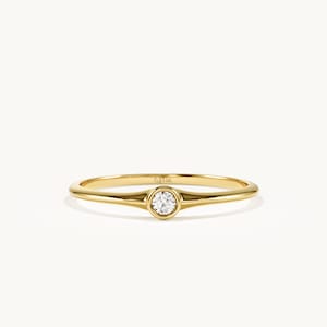 May include: A polished yellow gold ring featuring a single round brilliant-cut white diamond set in a bezel setting. The band is smooth and slender, with the hallmark 14K stamped clearly on the inner surface of the gold metal ring band.