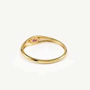 May include: A gold ring featuring a smooth, polished band and a small, oval-shaped setting at the top. The setting contains a single, vibrant pink gemstone that is securely held within the gold metal frame, creating a simple and elegant design.