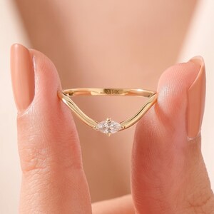 May include: A gold V-shaped ring featuring a single marquise-cut clear gemstone at the center point. The band is polished yellow gold and includes a clear 14K stamp on the inner surface, indicating the gold purity of the metal band.