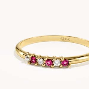 May include: A thin yellow gold ring featuring a row of six alternating round-cut clear white stones and vibrant pink stones set in a prong setting. The interior of the smooth, polished gold band is clearly stamped with the text 14K.