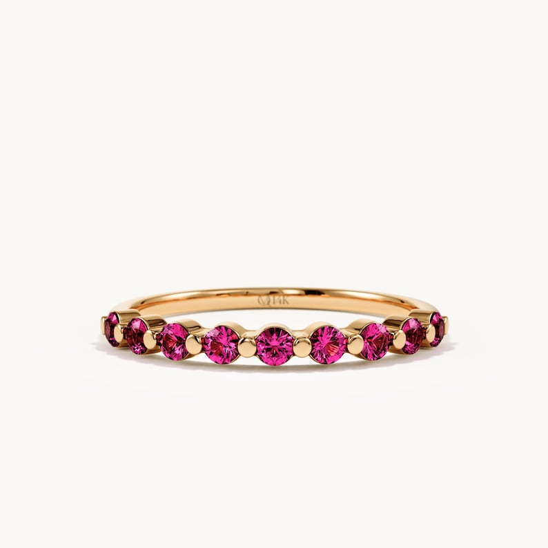 K&ouml;nnte beinhalten: Ein Goldring mit einer Reihe von neun rund geschliffenen, leuchtend pinkfarbenen Edelsteinen in einer gemeinsamen Krappenfassung. Auf der Innenseite des Rings ist deutlich die Gravur 14K zu sehen, die den Goldgehalt des Schmuckst&uuml;cks angibt.