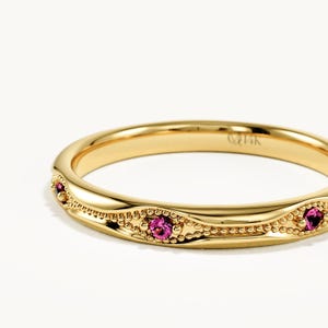 Peut inclure: Une bague en or jaune ornée d'une série de petites pierres précieuses roses rondes serties dans un motif ondulé perlé sur la surface extérieure. L'intérieur de l'anneau porte l'inscription 14K, indiquant la pureté de l'or.