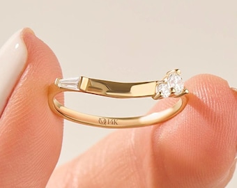 May include: A 14K gold ring featuring a curved band with a single baguette-cut diamond on one side and two round brilliant-cut diamonds on the other. The band is engraved with the text 14K on the inner surface, showcasing a polished finish.