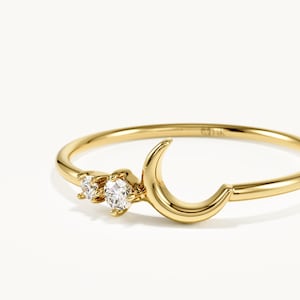 Op de afbeelding: Een dunne gouden ring met een gepolijste halve maanvorm en twee kleine, ronde, heldere gefacetteerde stenen die naast elkaar bij de maan zijn geplaatst. De ringband is glad en rond, met de tekst 14K duidelijk gegraveerd aan de binnenzijde.