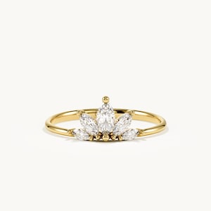 May include: A gold ring featuring a central marquise-cut clear gemstone flanked by four smaller marquise-cut clear gemstones arranged in a fan-like pattern. The band is thin and polished gold, with small gold spheres placed between the stones.