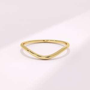 May include: A polished yellow gold ring with a smooth, curved V-shape band. The metal surface is reflective and features a small, clear 14K hallmark stamp on the inner side of the band, indicating the gold purity of the jewelry piece.