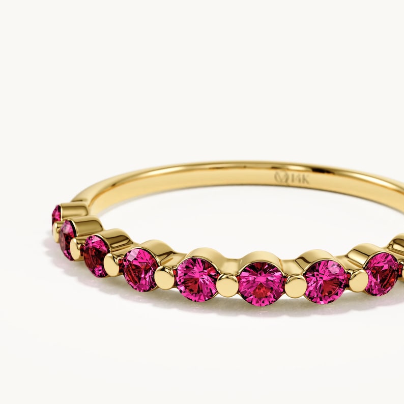 K&ouml;nnte beinhalten: Ein Ring aus Gelbgold mit einer Reihe runder, facettierter, leuchtend pinker Edelsteine in einzelnen Fassungen. Auf der Innenseite des Rings ist deutlich der Text 14K eingraviert, der den Reinheitsgrad des Goldes angibt.