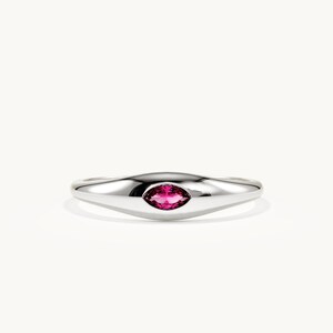 May include: A polished silver-tone ring featuring a smooth, tapered band and a single marquise-cut vibrant pink gemstone set horizontally in the centre. The metal surface has a high-shine finish that reflects light across the curved band.