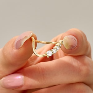 May include: A gold ring featuring a curved, open-ended band with five round, clear stones set along one side. The inner surface of the band is clearly stamped with the text 14K, indicating the metal purity of this piece of fine jewelry.