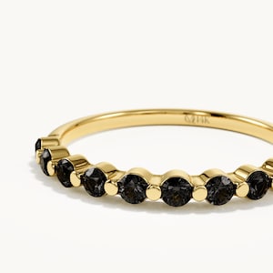 May include: A yellow gold ring featuring a row of round, dark grey stones set in a shared prong design. The inner band is clearly stamped with the text 14K, indicating the metal purity. The stones are arranged in a continuous line along the front.