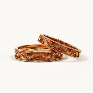 Pu&ograve; includere: Due anelli in oro con un motivo a onde ripetuto, bordi con perline sottili e incisioni a raggiera. L'interno dell'anello piatto &egrave; chiaramente stampigliato con il testo 14K, che indica la purezza dell'oro di queste fasce in metallo lucido.