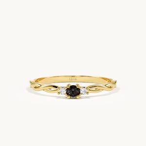 May include: A yellow gold ring featuring a central dark grey round-cut gemstone flanked by two smaller clear round-cut gemstones. The band has a twisted, rope-like design on both sides of the stones, and the interior is stamped with 14K.