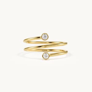 May include: A gold bypass ring featuring a spiral design with two round, bezel-set clear stones at each end. The band is polished yellow gold, and the metal is stamped with the text 14K on the inner surface of the spiral coil.