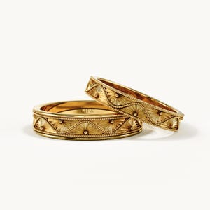 Pu&ograve; includere: Due anelli in oro giallo caratterizzati da un motivo a onde ripetuto e testurizzato, bordi perlati e incisioni a raggiera. L'interno dell'anello piatto reca chiaramente l'incisione 14K, che indica la purezza dell'oro delle fasce.