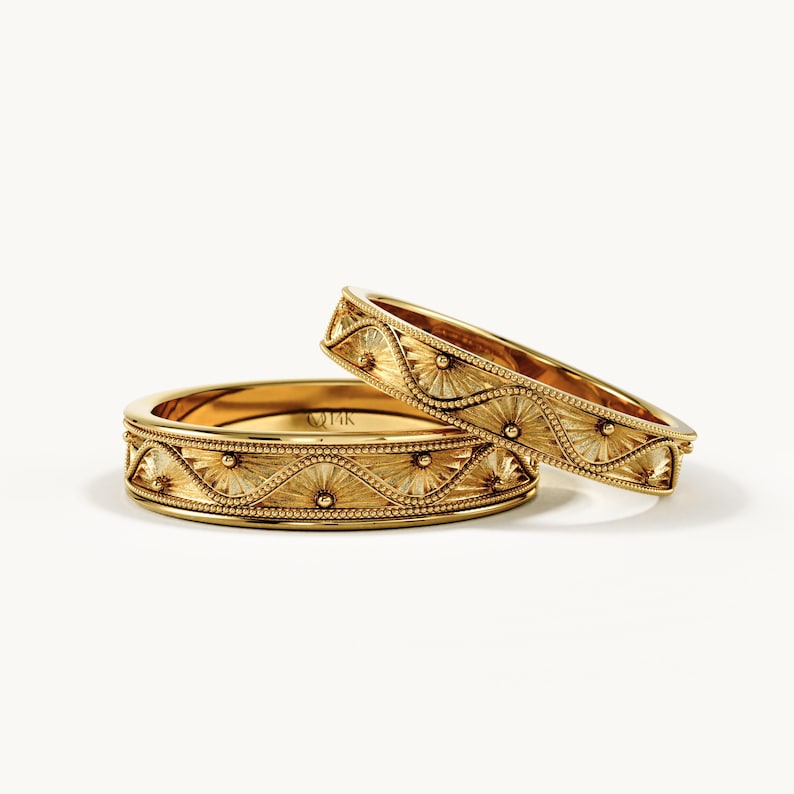 Pu&ograve; includere: Due anelli in oro giallo caratterizzati da un motivo a onde ripetuto e testurizzato, bordi perlati e incisioni a raggiera. L'interno dell'anello piatto reca chiaramente l'incisione 14K, che indica la purezza dell'oro delle fasce.