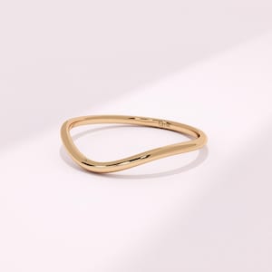 May include: A gold-colored ring with a unique, wavy design. The ring has a smooth, polished surface and a minimalist aesthetic. The ring is a piece of jewelry.