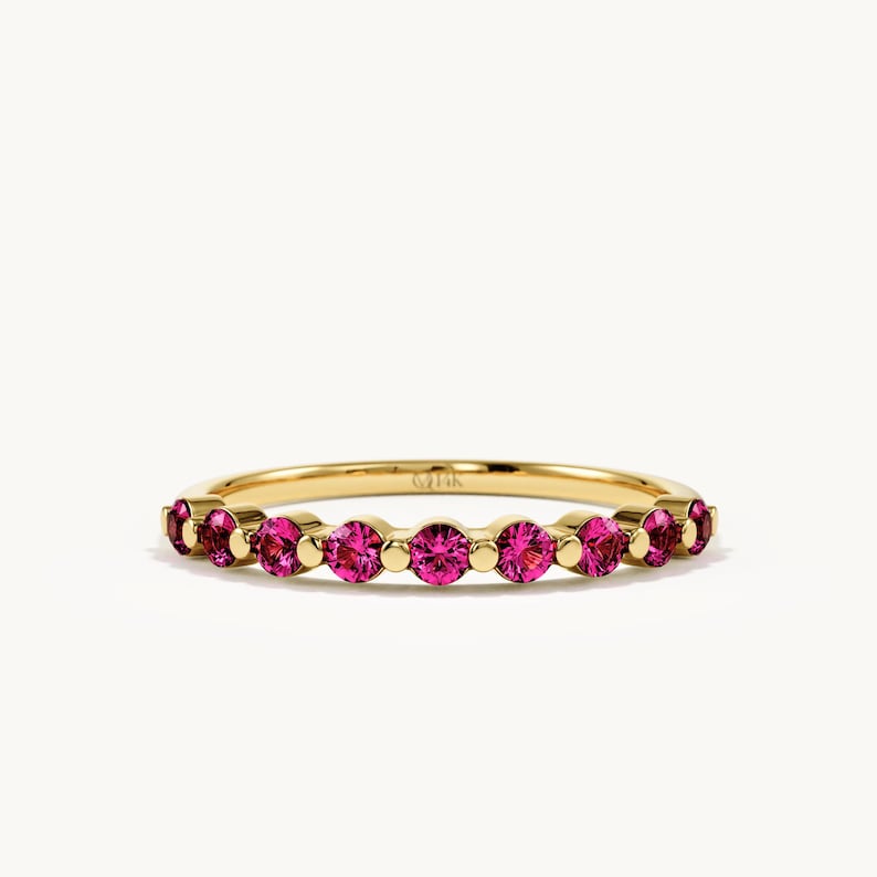K&ouml;nnte beinhalten: Ein Ring aus Gelbgold mit einer Reihe von rund geschliffenen, leuchtend pinkfarbenen Edelsteinen in einer gemeinsamen Krappenfassung. Die Innenseite des d&uuml;nnen Metallrings ist deutlich mit der Gravur 14K versehen, die den Goldgehalt angibt.
