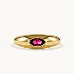 May include: A polished gold band ring featuring a central marquise-cut vibrant pink gemstone set horizontally. The ring has a smooth, rounded, and thick profile that tapers slightly toward the edges, highlighting the faceted pink stone.