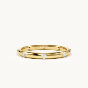 May include: A polished yellow gold band ring featuring multiple round, clear, faceted stones set at intervals along the outer surface. The interior of the band is clearly engraved with the text 14K, indicating the metal purity of the jewellery piece.