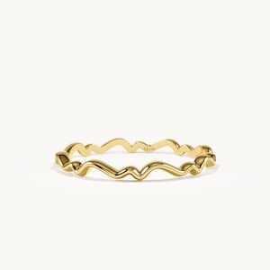 Può includere: Un anello in oro giallo lucido caratterizzato da un design ondulato fluido e continuo che circonda l'intera fascia. La superficie metallica è liscia e riflettente, con la piccola e chiara incisione 14K visibile sul lato interno dell'anello.