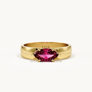 May include: A gold band ring featuring a marquise-cut vibrant pink gemstone set in the centre. The interior of the band is clearly stamped with the text 14K, indicating the metal purity. The ring has a polished finish and a smooth, rounded band.
