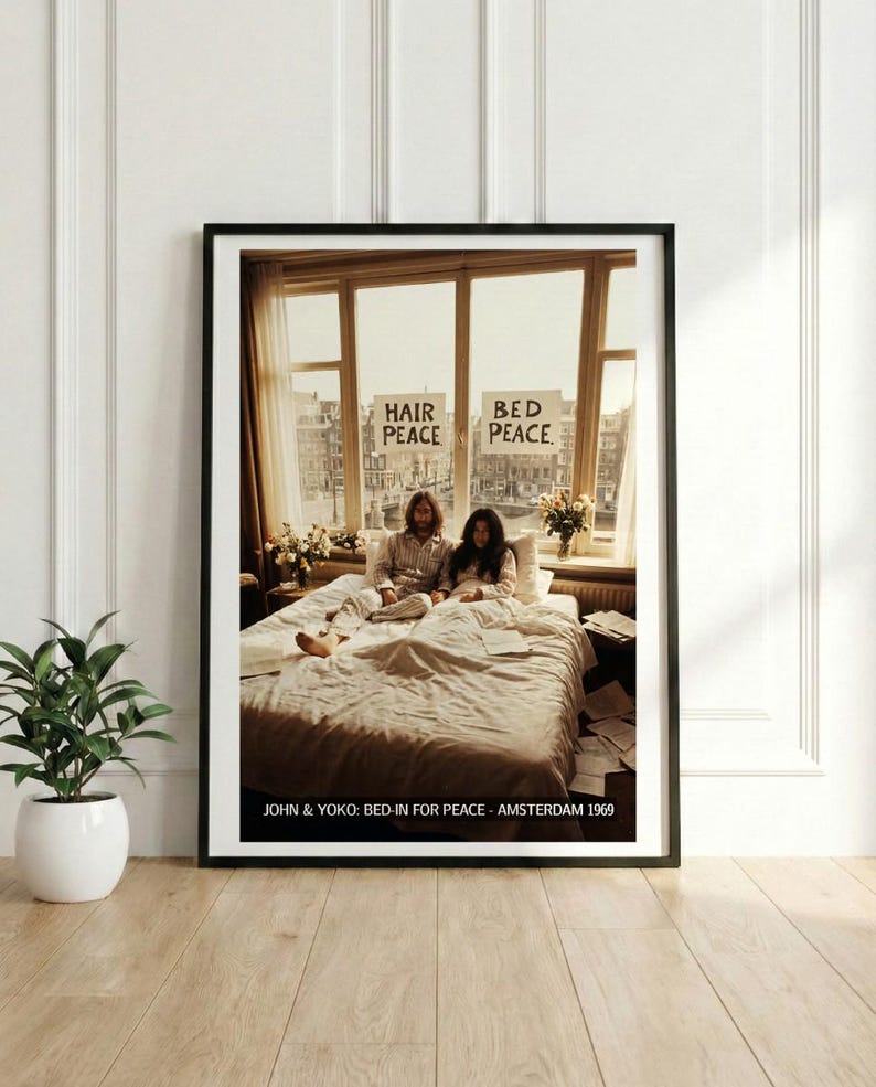May include: Framed print featuring John Lennon and Yoko Ono in bed, with signs reading "Hair Peace" and "Bed Peace." The image is from their Bed-In for Peace in Amsterdam, 1969. The print is in a black frame, with a white border.