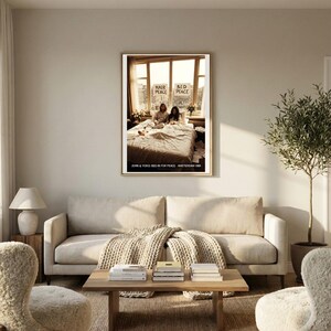 May include: A framed print featuring a photograph of John Lennon and Yoko Ono in bed, with the words "Hair Peace Bed Peace" visible. The print is displayed above a light-colored sofa in a living room setting.