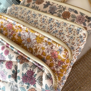 May include: Four quilted zippered pouches with floral patterns in shades of pink, blue, yellow, and brown. The pouches are stacked on top of each other, with the top pouch being the most visible.
