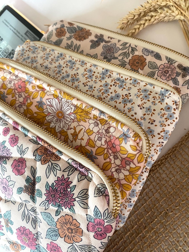 May include: Four quilted zippered pouches with floral patterns in shades of pink, blue, yellow, and brown. The pouches are stacked on top of each other, with the top pouch being the most visible.