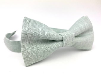 May include: A light gray linen bow tie. The bow tie is made of a soft, textured fabric.