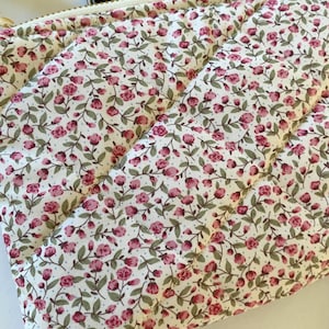 May include: A quilted zippered pouch with a white background and a small pink floral pattern. The pouch is made of a soft fabric and has a zipper closure.