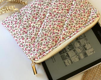 May include: A white quilted zippered pouch with a floral print featuring small pink flowers. The pouch is open and a black e-reader is inside.