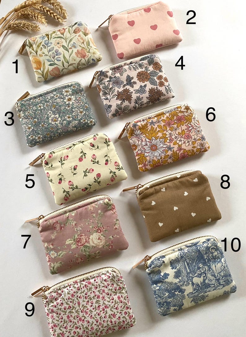 May include: A collection of ten small, rectangular zippered pouches. The pouches feature various floral, heart, and toile patterns in shades of pink, blue, and brown. Each pouch has a gold-toned zipper and a small leather pull.