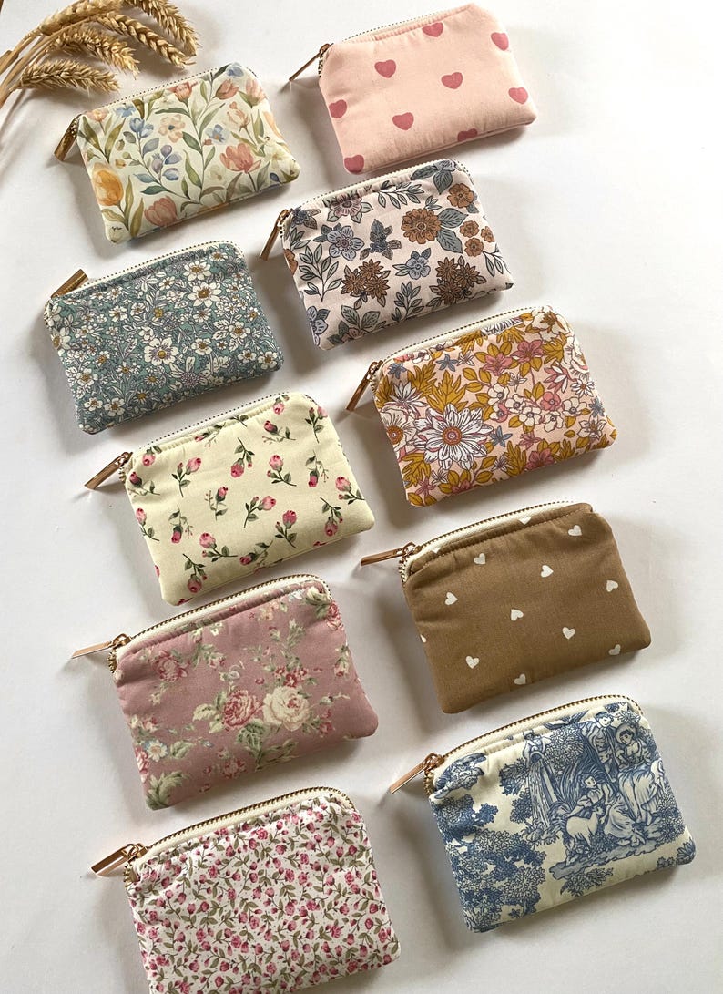 May include: A collection of small, rectangular fabric pouches with zippers. The pouches feature various floral and patterned designs in colors like pink, blue, and brown. Some have heart patterns, while others showcase classic floral prints.