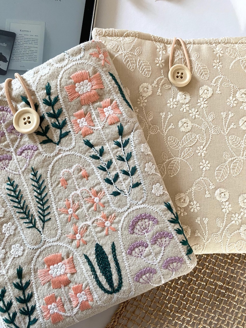Pu&ograve; includere: Due pochette in lino beige con motivi floreali ricamati. La pochette a sinistra presenta un design pi&ugrave; dettagliato con fiori rosa, verdi e viola. La pochette a destra presenta un design pi&ugrave; semplice con fiori bianchi. Entrambe le pochette hanno una chiusura a bottone.