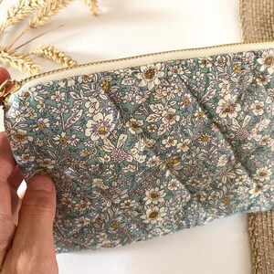 May include: A quilted pouch with a floral pattern in shades of blue, white, and yellow. The pouch has a gold zipper and a rectangular shape. The floral design is a repeating pattern of small flowers and leaves.