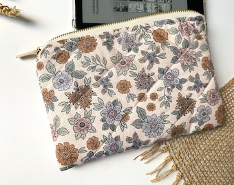 Puede incluir: Una bolsa de cremallera beige con un estampado floral con flores marrones, rosas y azules. La bolsa está acolchada y tiene una cremallera dorada.
