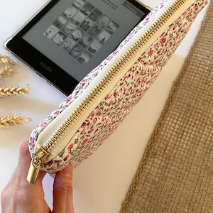 May include: A white zippered pouch with a floral pattern featuring pink roses. The pouch is made of quilted fabric and has a gold zipper.
