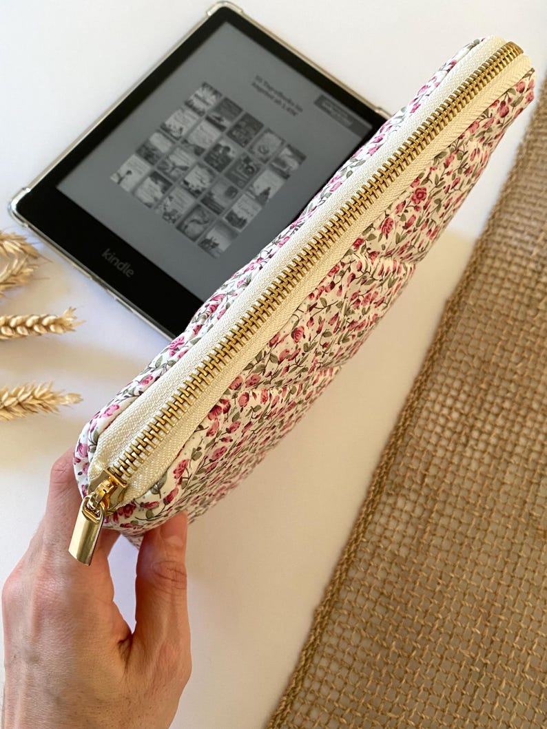 May include: A white zippered pouch with a floral pattern featuring pink roses. The pouch is made of quilted fabric and has a gold zipper.