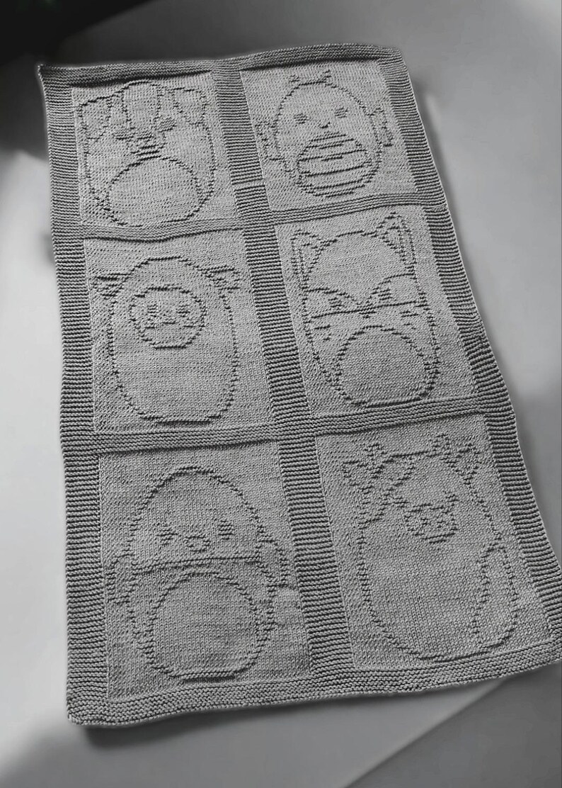 May include: A gray knitted baby blanket featuring six squares, each with a different animal face design. The animals include a bear, a bird, a cat, a pig, and two other creatures. The blanket has a ribbed border.