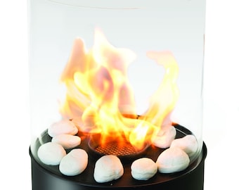 May include: A tabletop fireplace with a black base and a clear glass cylinder. Inside, flames dance above white stones. The design is modern and creates a warm ambiance. The fireplace is a decorative home accessory.