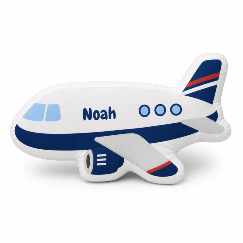 May include: A white airplane-shaped pillow with blue and red accents. The pillow features the name "Noah" in blue lettering, along with blue windows and three blue circles. The wings and tail have blue and red details.