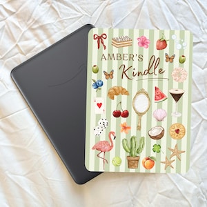 May include: A black Kindle e-reader with a decorative cover. The cover features a light green and white striped design with watercolour illustrations of various objects. The text "AMBER'S Kindle" is displayed on the cover.