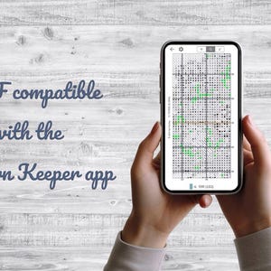 May include: A smartphone displays a cross-stitch pattern, held against a light wood background. The screen shows a grid with colored squares. Text on the screen reads "a 500 stitches". The text "PDF compatible with the Pattern Keeper app" is also visible.