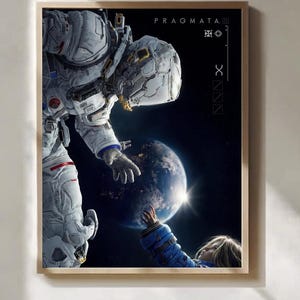 May include: A framed wall art print featuring an astronaut in a white suit reaching toward a child in a blue jacket against a dark space background with a glowing planet Earth. The text PRAGMATA is printed in the upper right corner of the image.