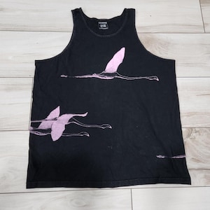 Puede incluir: Camiseta sin mangas negra con un diseño de flamenco rosa. La camiseta sin mangas presenta un cuello redondo y un diseño de flamencos volando. El gráfico del flamenco es de color rosa suave, creando contraste con la tela negra.