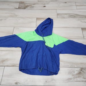 May include: A blue and green hooded jacket with a drawstring. The jacket has a color block design with a green band across the chest.